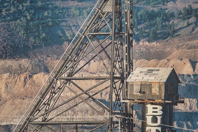2026 MIB Convention; A steel mining headframe towers against a rugged hillside, with "BUTTE" partially visible on the structure. The scene conveys industrial heritage.