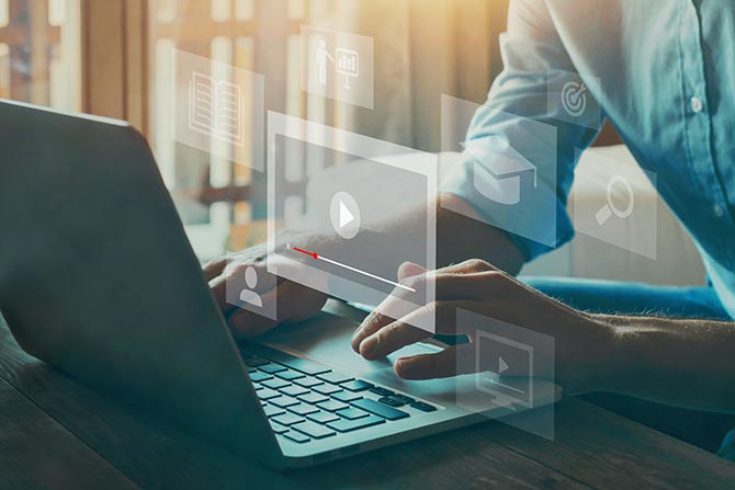 Bank Training Webinars; A person types on a laptop with glowing digital icons floating above, suggesting tech interaction. Sunlight streams in, creating a focused atmosphere.